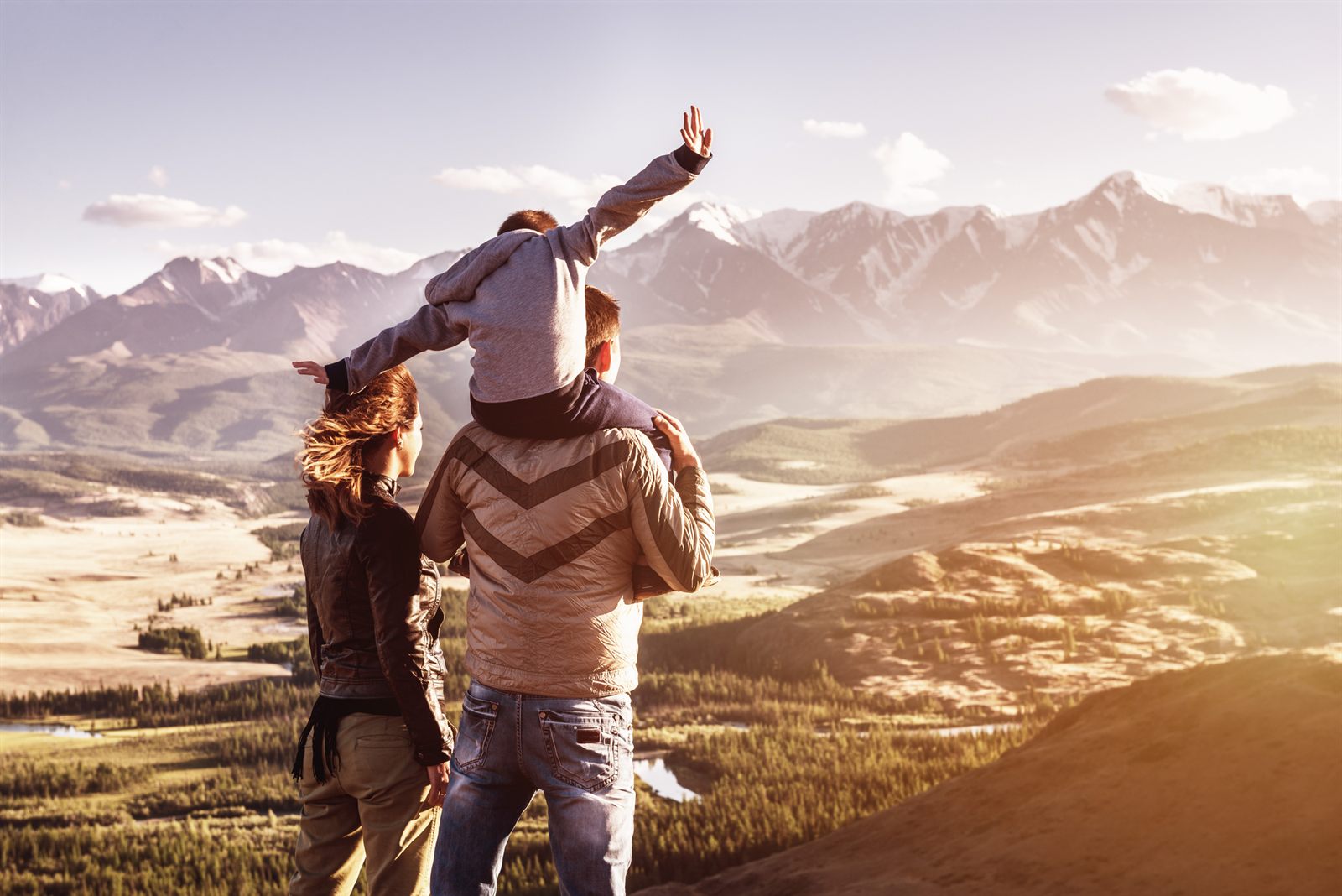 Small child riding on a parent&rsquo;s shoulders above a mountain valley