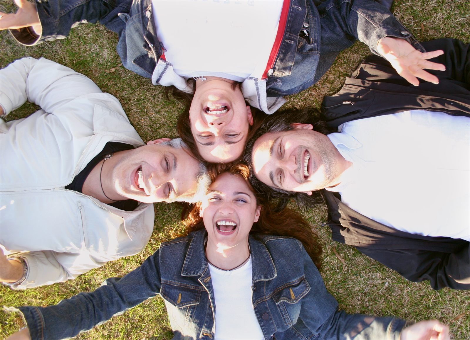Group of smiling teenagers lying head to head on the grass